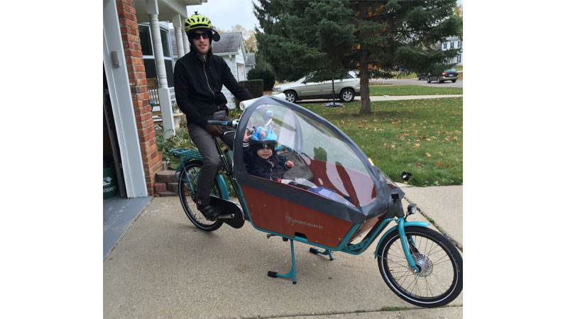 Jarin Marocco with son, Aurelio, ready to ride family cargo bike with weather guard cover. 