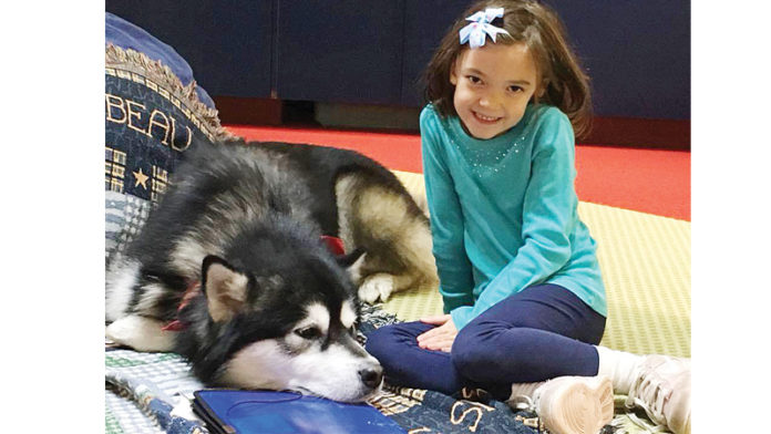 Kathryn, 8, pictured with service dog Hawkeye enjoying some reading time together during the READ program.