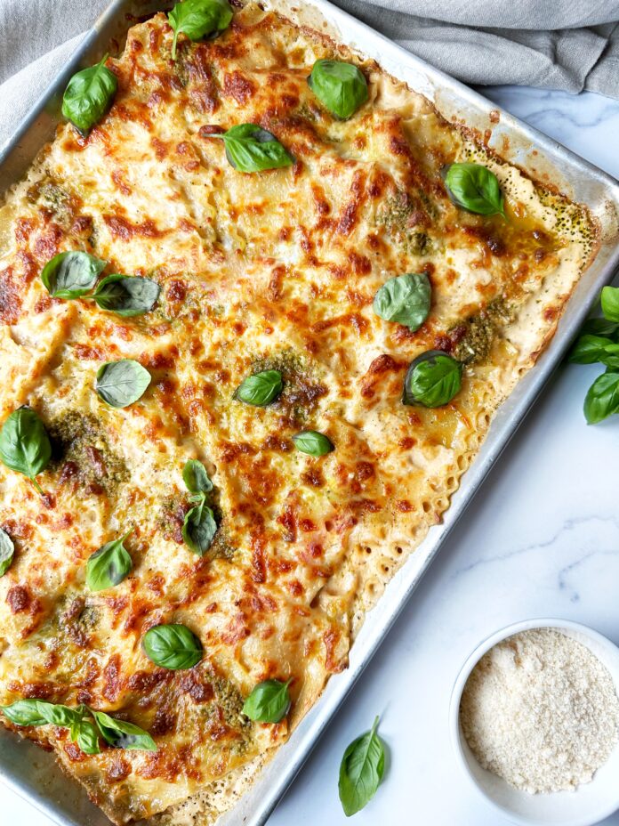 A sheet pan of pesto lasagna, a bowl of parmesan cheese, and some basil leaves.