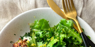 A shallow bowl of yogurt sauce topped with pearl couscous, meatballs and fresh greens.