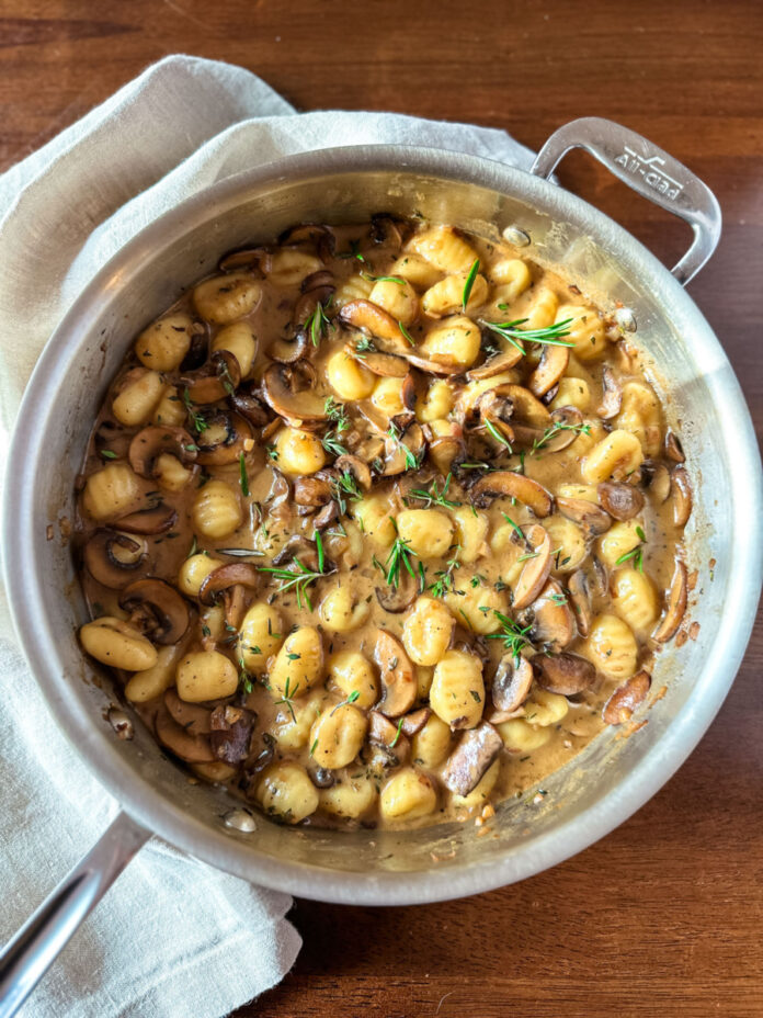 A large saute pan with gnocchi and mushrooms inside.