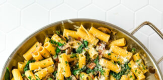 A saute pan filled with rigatoni pasta and bacon, mushrooms and spinach.