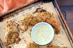 A sheet pan with pretzel-crusted chicken with honey-mustard dipping sauce next to an orange napkin.