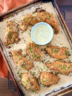 A sheet pan with pretzel-crusted chicken with honey-mustard dipping sauce next to an orange napkin.