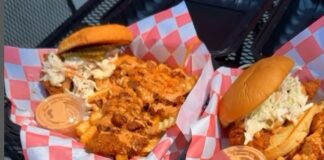 Three food baskets lined with red and white paper filled with spicy chicken sandwiches accompanied by a small container of an orange sauce.