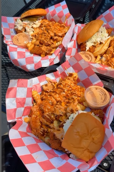 Three food baskets lined with red and white paper filled with spicy chicken sandwiches accompanied by a small container of an orange sauce.