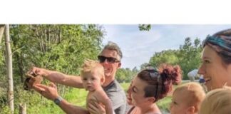 A joyful family poses on a dirt road, with a baby nestled in their arms, enjoying a sunny day outdoors
