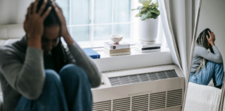 person sitting on ground by mirror with hands on face