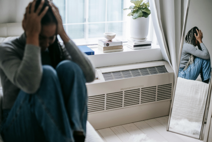 person sitting on ground by mirror with hands on face