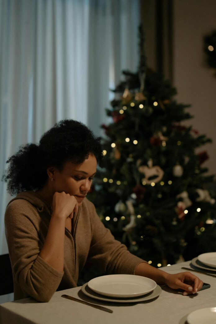 Sad woman at table by christmas tree