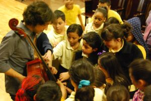 children gathered around to see and touch a cello.