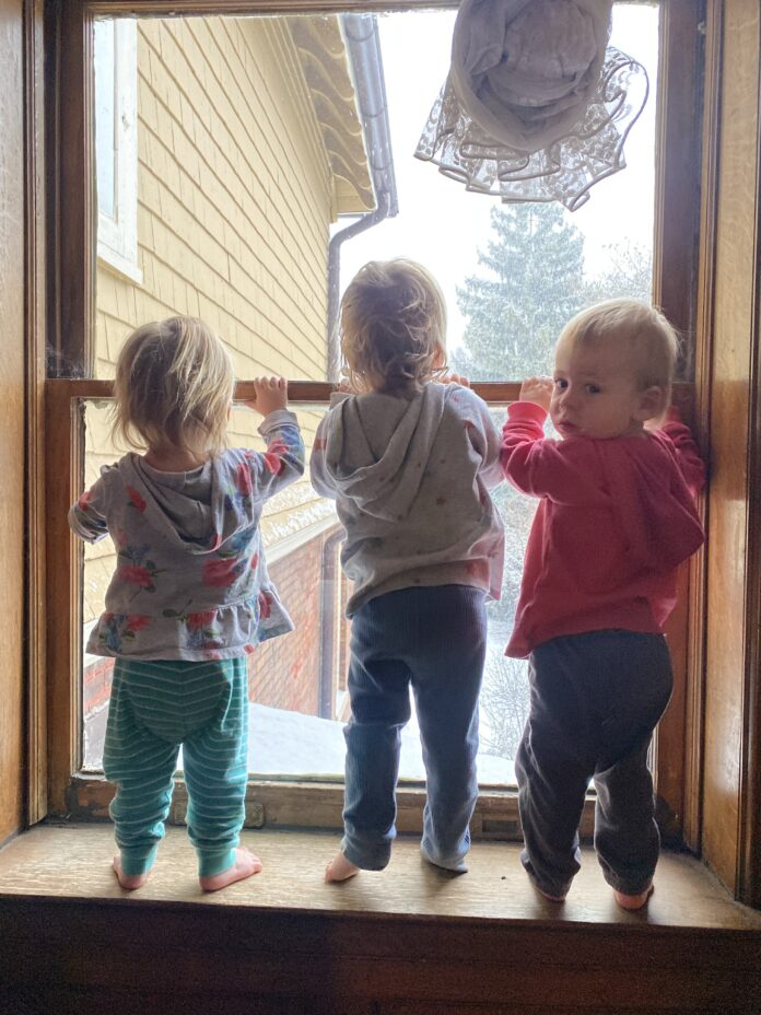 Triplets looking at window with one looking at camera