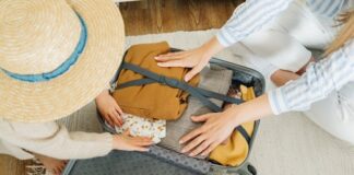 Two people packing a suitcase. One is wearing a hat