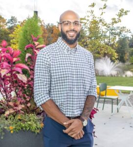 Quinn Coleman, founder of Casting Crowns, is a bald man of color with facial hair wearing a white and blue plain shirt and blue pants while standing outside.