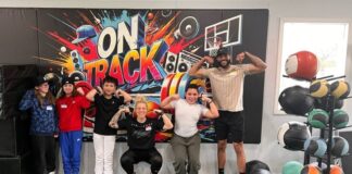 Adults and youth standing in front of a colorful banner that says "On Track" with gym equipment around them.