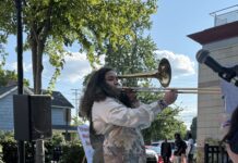 A young woman stands on an outside stage playing the trombone