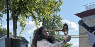A young woman stands on an outside stage playing the trombone