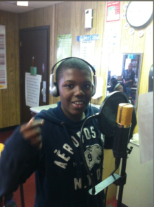 A young artists stands before a microphone recording his work.